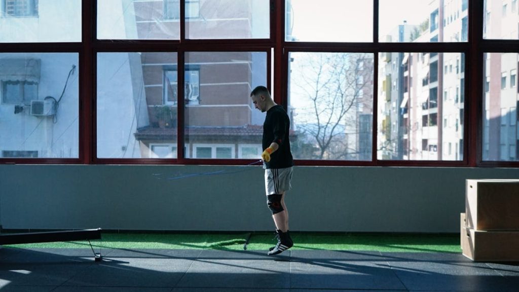Young man exercising with a skipping rope in an urban gym with large windows and city view.